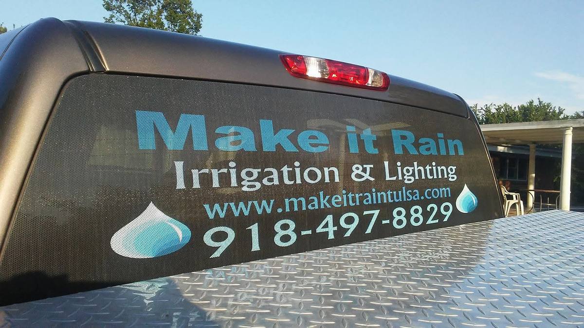 Rear window of a pickup truck lettered Make it Rain Irrigation & Lighting with a water-drop logo, website and phone number.